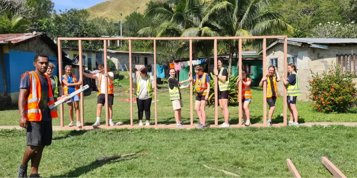 Ten volunteers wearing orange and green high-vis jackets pose for a picture as they build a wooden frame.