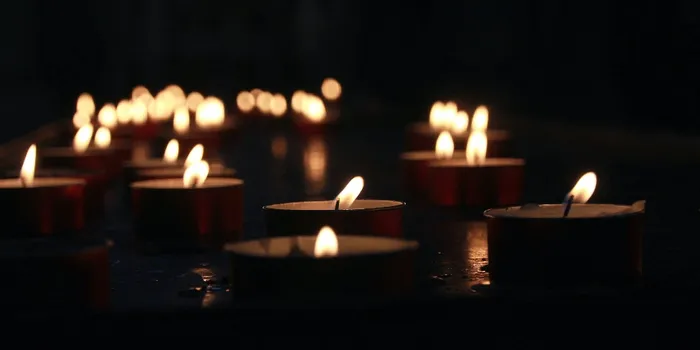 A number of lit tea light candles in a dark space