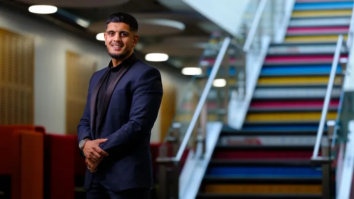 A male wearing a blue suit stands at the bottom of a multi-coloured staircase