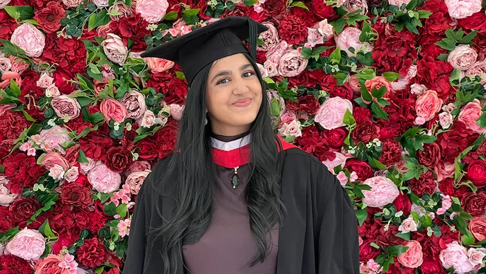 A student in cap and gown posing in front of a wall of red and pink roses.