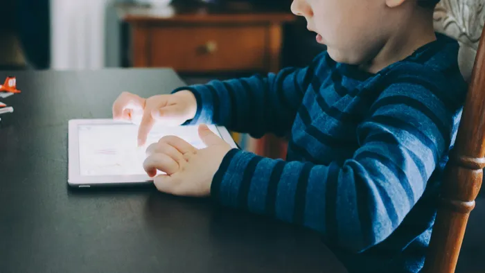 A young child sitting at a table and using a tablet.