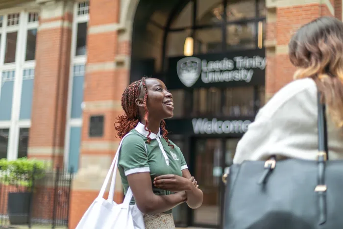 Two students talking and laughing outside the Leeds City Campus entrance.