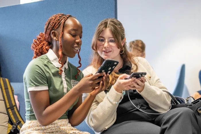 Students in Leeds City Campus social space looking at their phones.
