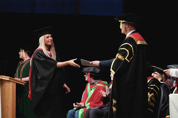Student shaking hands with executive during graduation ceremony.